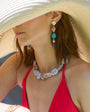 Woman wearing a straw hat, red top, and colorful jewelry on a beach.