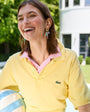 Woman in yellow polo shirt with pink collar wearing gold and charm earrings holding a striped beach ball outdoors.