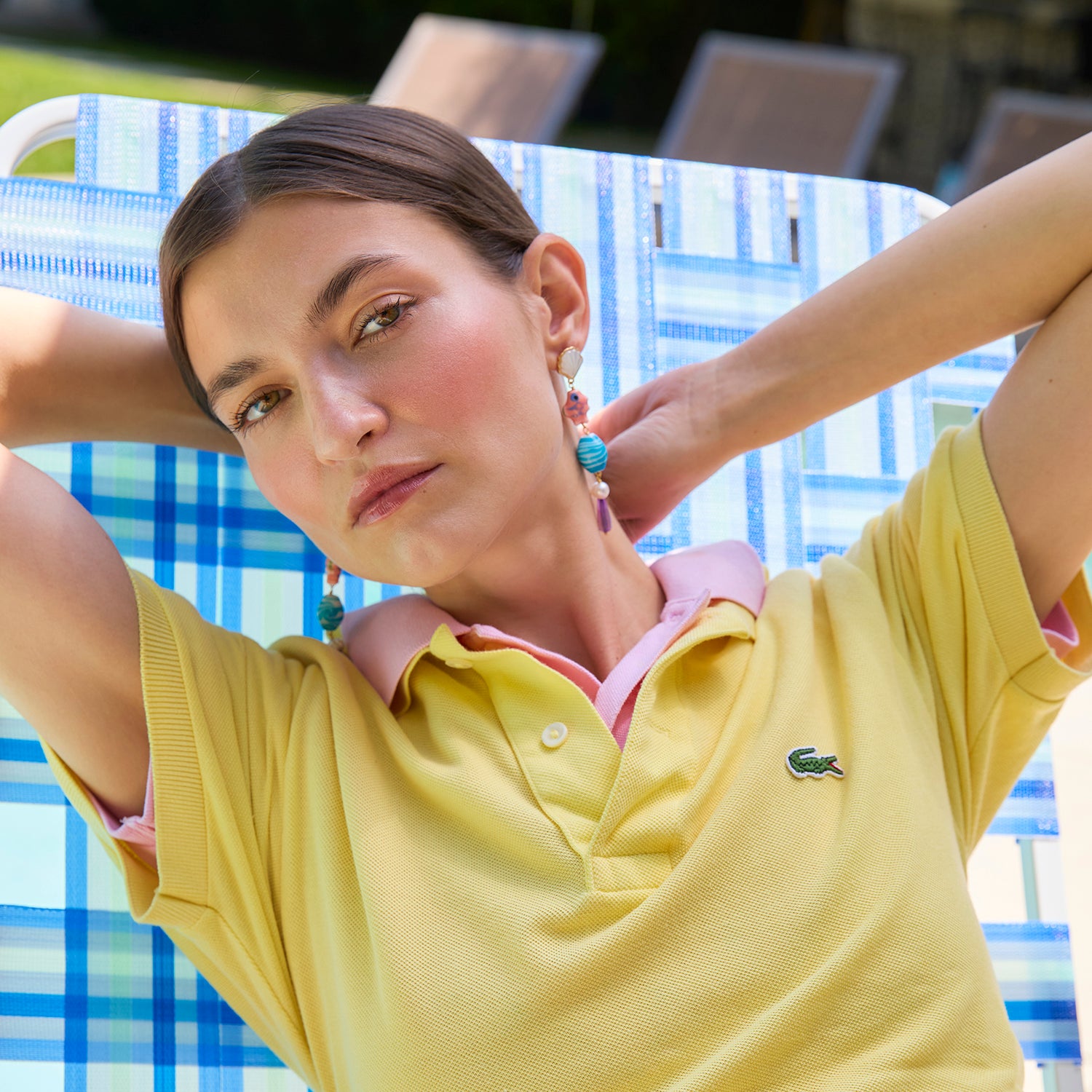 Woman wearing a yellow polo shirt with a visible brand logo, sitting on a blue and white checkered chair.