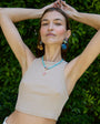Woman wearing a beige top with colorful jewelry against a green leafy background