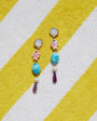 Colorful earrings with shell and fish designs on a yellow and white striped fabric background