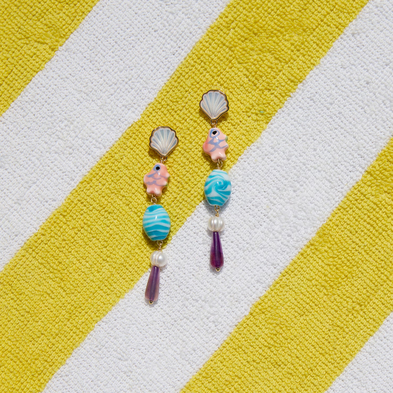Colorful earrings with shell and fish designs on a yellow and white striped fabric background