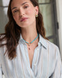 Woman wearing a light blue striped shirt with a necklace and earrings indoors.