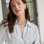 Woman wearing a light blue striped shirt with a necklace and earrings indoors.
