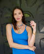 Woman wearing a blue top with beaded and gold jewelry against a decorative dark background