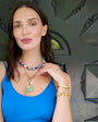 Woman wearing colorful and beaded jewelry against a decorative wall.
