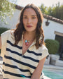 Woman wearing a cream and navy striped vest with a gold collar necklace featuring fish charms with a blurred outdoor background