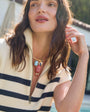 Woman wearing a cream and navy striped vest with a gold collar necklace featuring fish charms with a blurred outdoor background