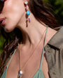 Close-up of a woman wearing colorful earrings and a necklace with a blurred natural background