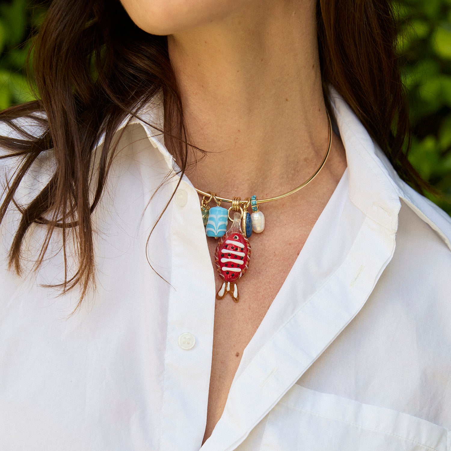 Necklace with colorful charms worn by a person in a white shirt.