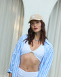Woman wearing a white top and blue striped shirt with a beaded necklace, outdoors.
