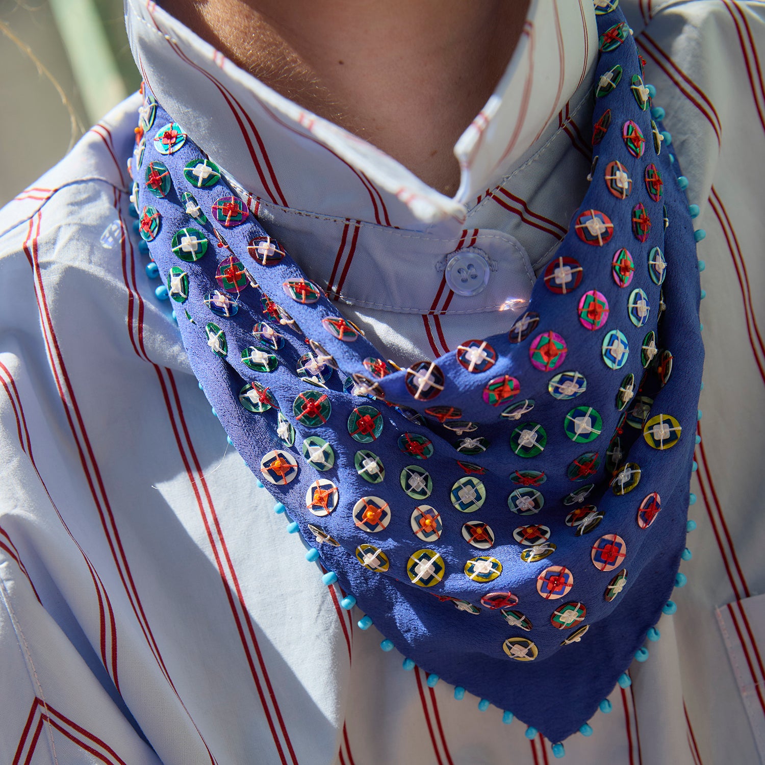 Model wearing blue and sequin emboidered scarf around her neck with a striped shirt 