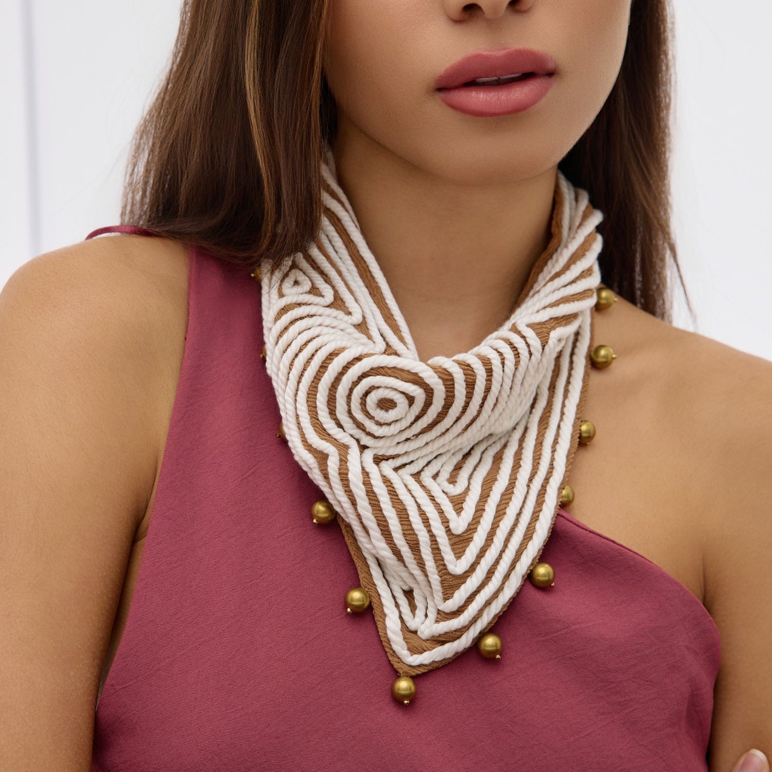 Woman wearing a decorative scarf with gold beads on a plain background