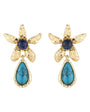 A pair of gold flower-shaped drop earrings featuring a round dark blue cabochon stone at the center and a teardrop-shaped turquoise stone hanging below, set against a plain white background.