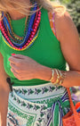 Woman in a green top with colorful necklace and patterned skirt, holding an orange bag, standing in a garden.