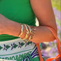 Woman in a green top with colorful necklace and patterned skirt, holding an orange bag, standing in a garden.