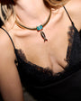 Close-up of a person wearing a gold necklace with a blue gem and fish pendant, and a black lace top.