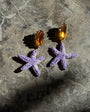 Purple starfish-shaped earrings on a textured stone surface