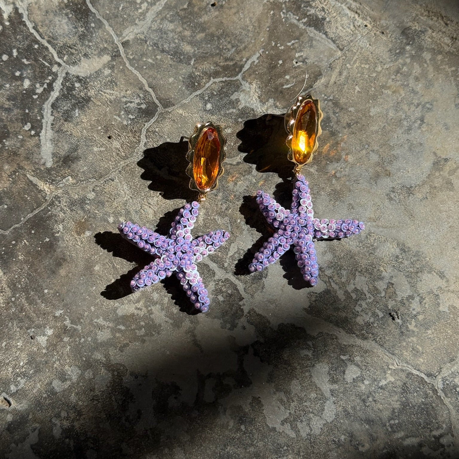 Purple starfish-shaped earrings on a textured stone surface