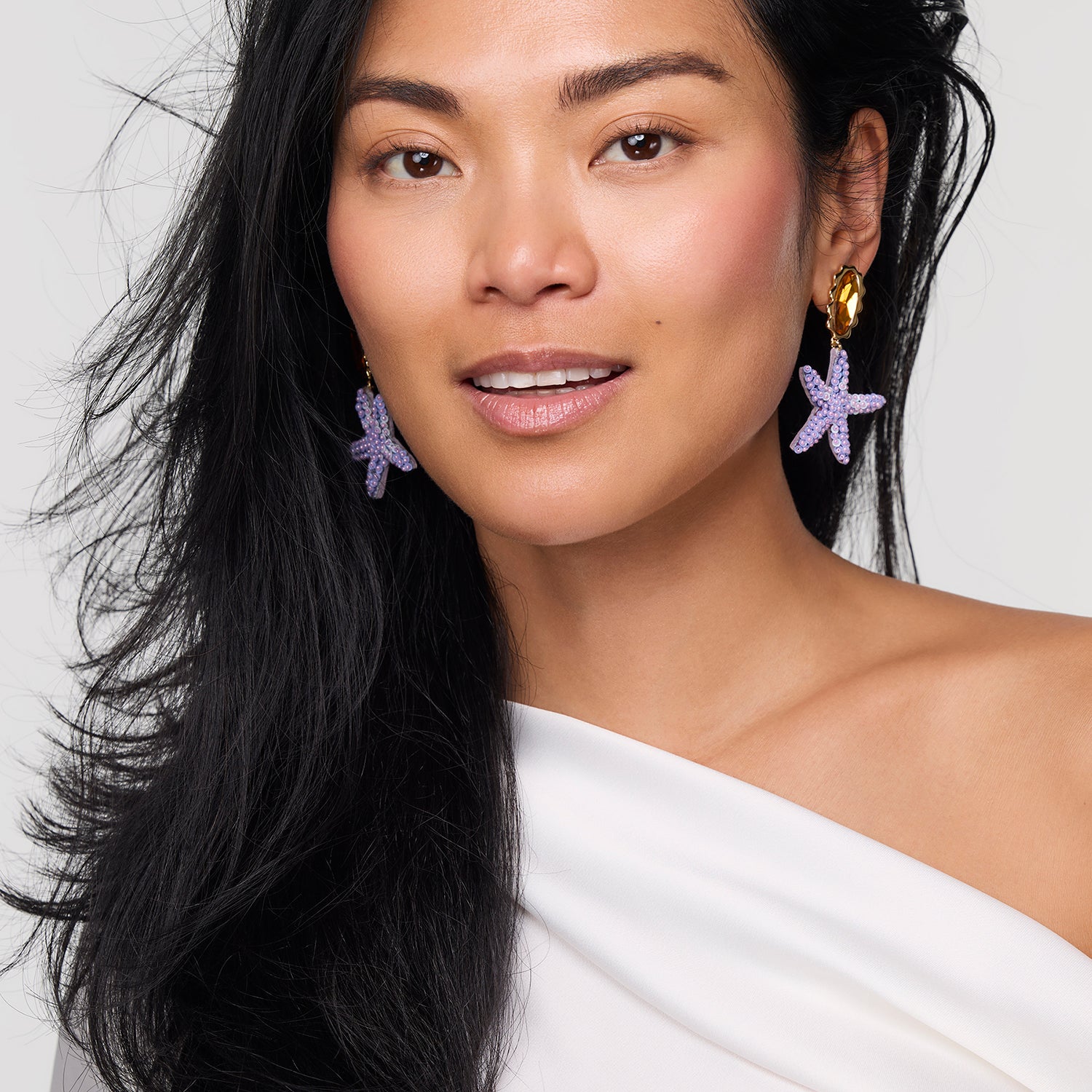 Woman wearing starfish-shaped earrings against a plain background