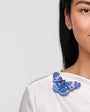 Woman wearing a white top with a blue butterfly brooch accessory on a plain background