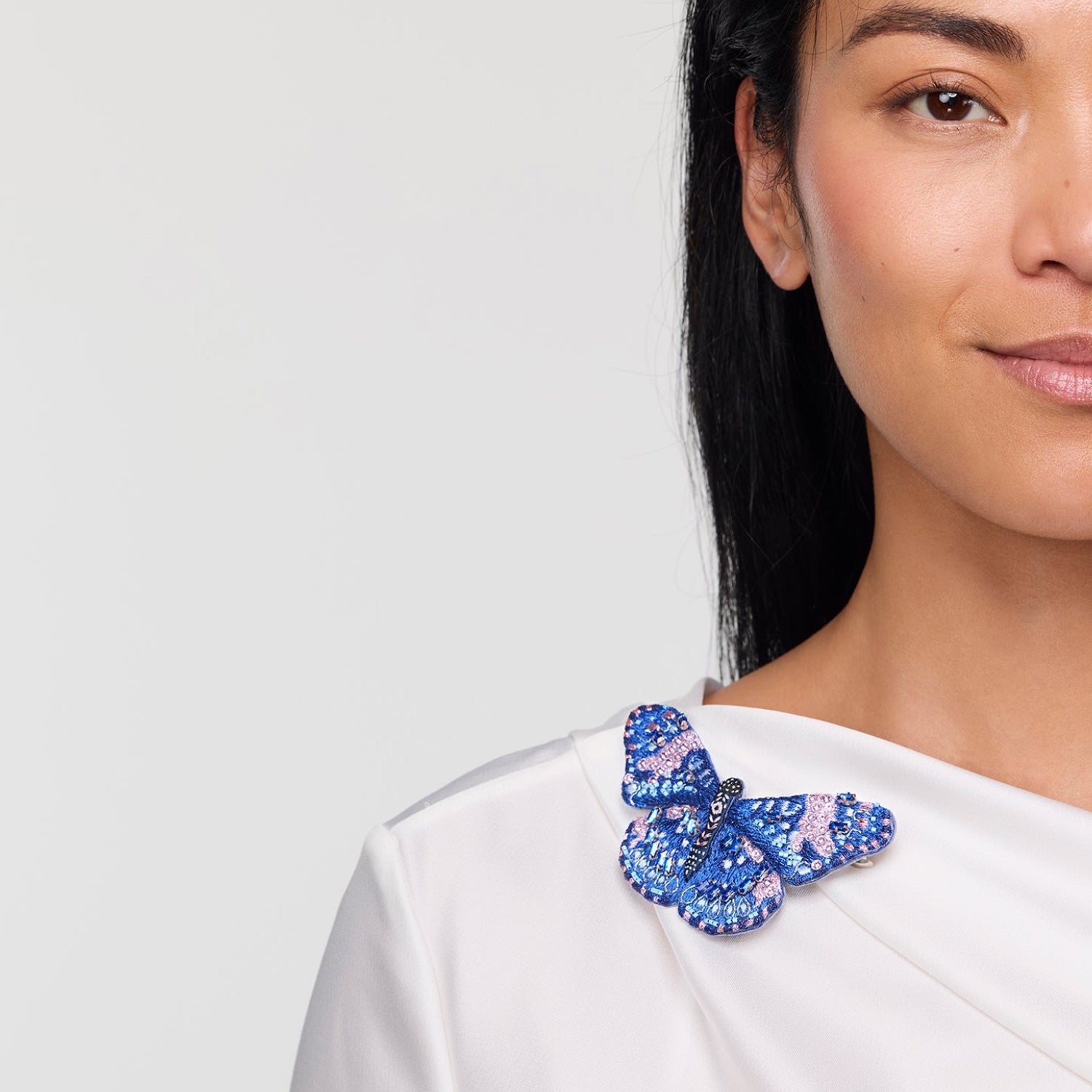 Woman wearing a white top with a blue butterfly brooch accessory on a plain background
