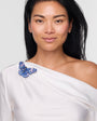 Woman wearing a white off-shoulder top with a blue butterfly brooch accessory on a plain background