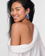 Woman with butterfly earring in ear while wearing a  white garment draped over her shoulders against a plain background