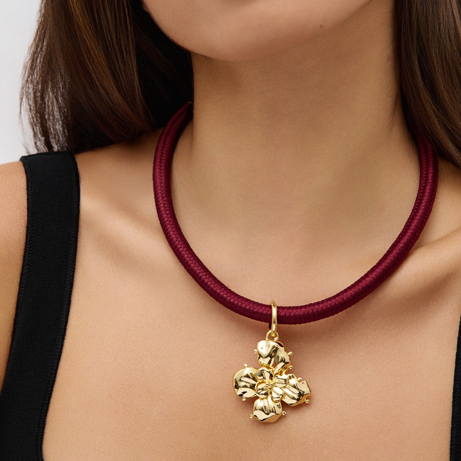Gold necklace with a red cord and gold pendant on a person wearing a black top.