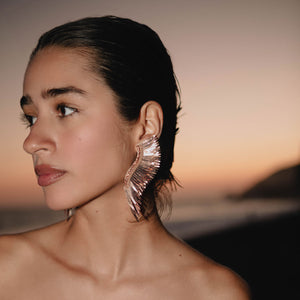 Metallic Rose Gold Wing Earrings Styled on Model at the Beach During Sunset