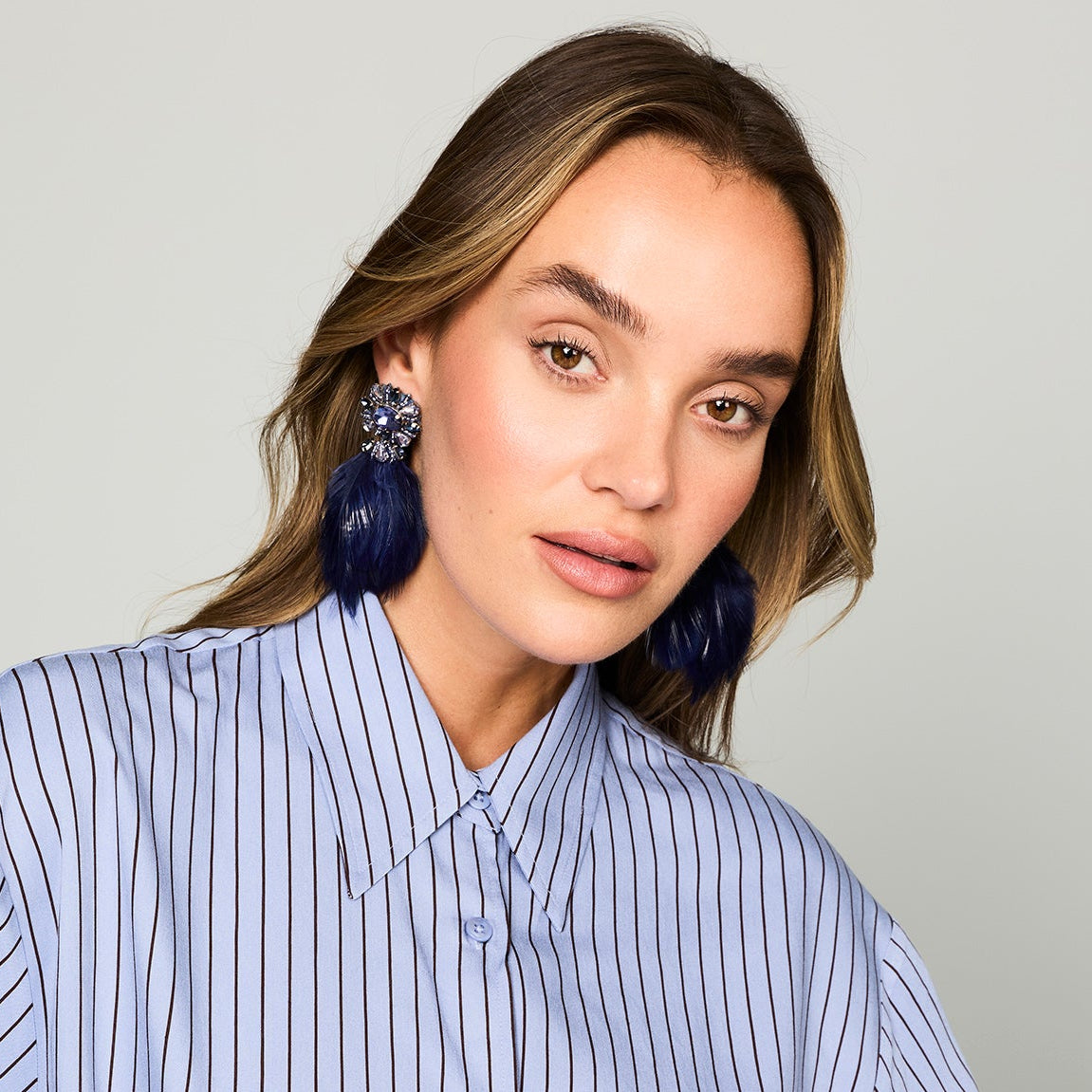 Navy feather drop earrings with ornate floral-inspired tops and gold-tone details on model head tilted down