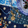 A styled flat-lay of jewelry and accessories, featuring a gold necklace with celestial pendants, blue beaded necklaces, gold and blue earrings, and a blue patterned textile on a white and blue surface.