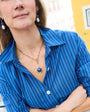 Model wearing a long gold chain necklace with a blue stone pendant wearing a striped blue shirt