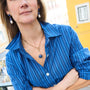 Model wearing a long gold chain necklace with a blue stone pendant wearing a striped blue shirt