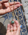 A gold chain necklace with a central green marbled stone pendant and small clear stones, held in a person's hand against a blue and white tiled background.