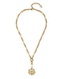 A gold chain necklace featuring a unique elongated link design and a central flower-shaped pendant with a textured center, displayed on a clean white background.