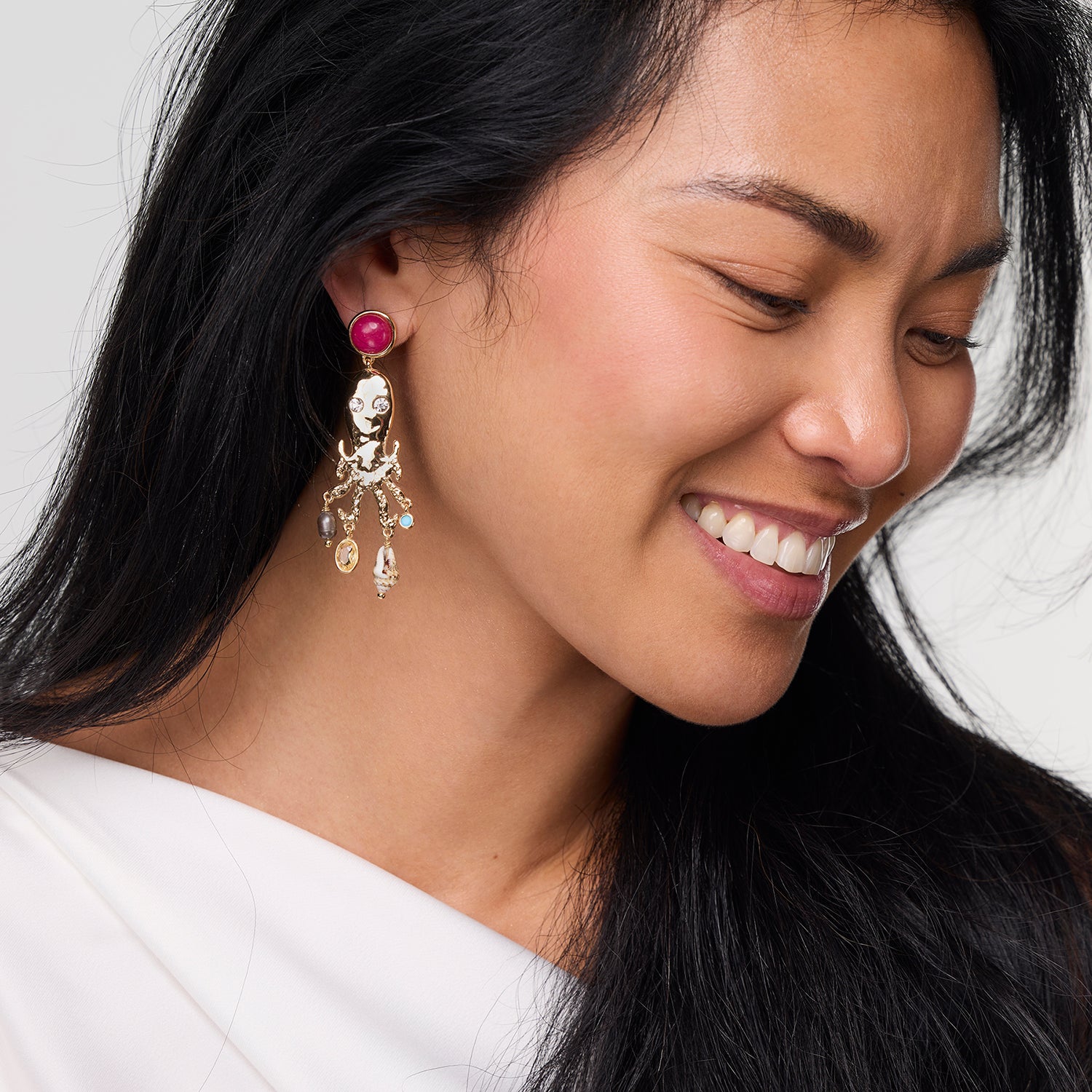 Close-up of a woman wearing a decorative earring with a red gemstone on a white background