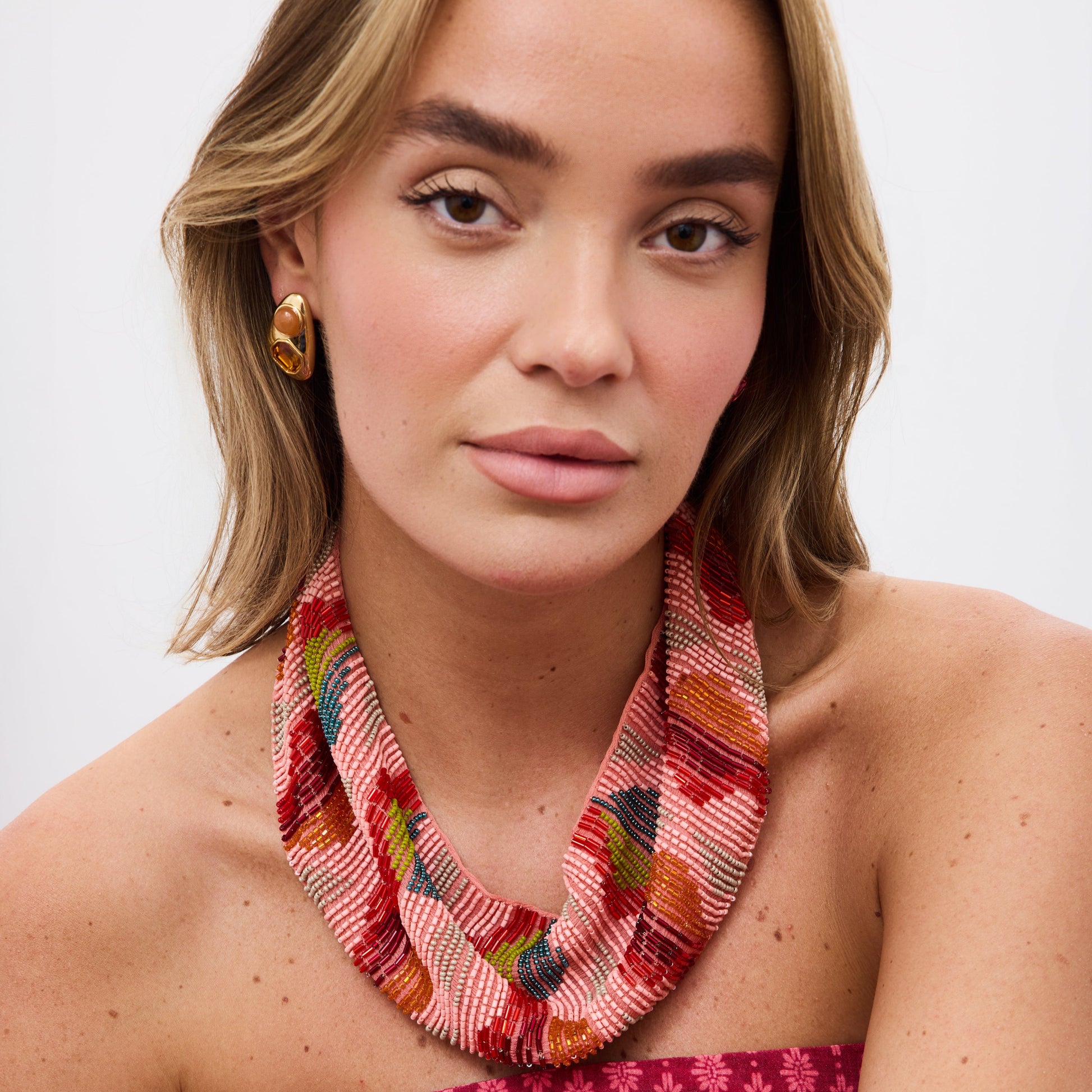 Woman wearing a colorful necklace and pink patterned dress against a white background