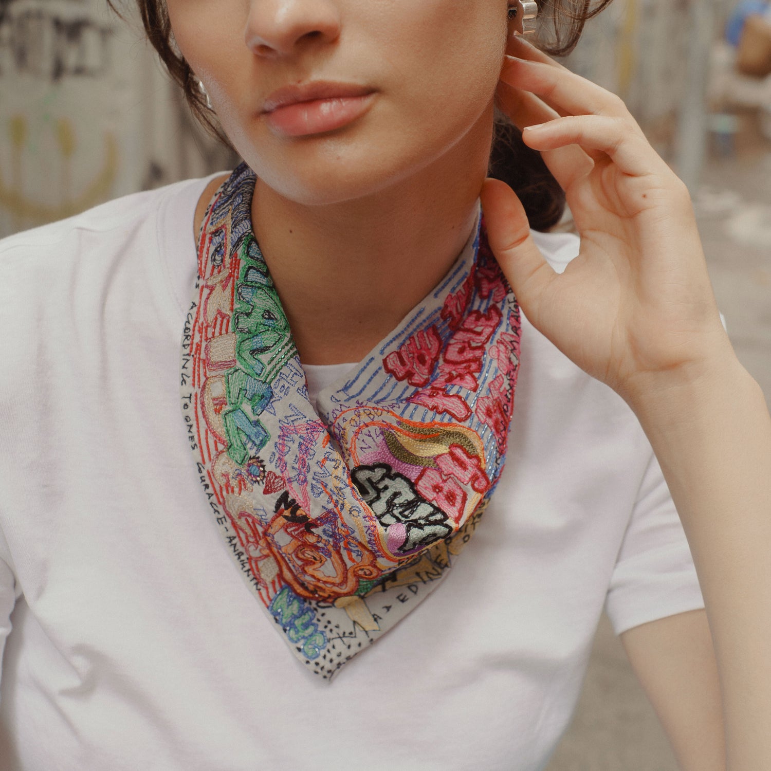 A close-up lifestyle shot of a model wearing a white t-shirt and a colorful, patterned neck scarf with a vintage map design.