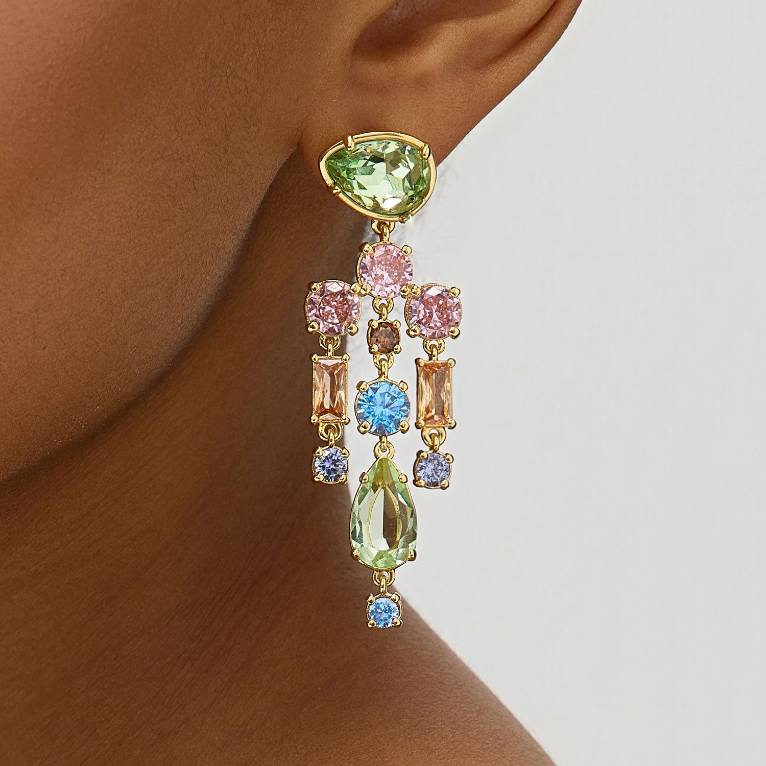 Multicolored gemstone earrings on a person's ear against a neutral background