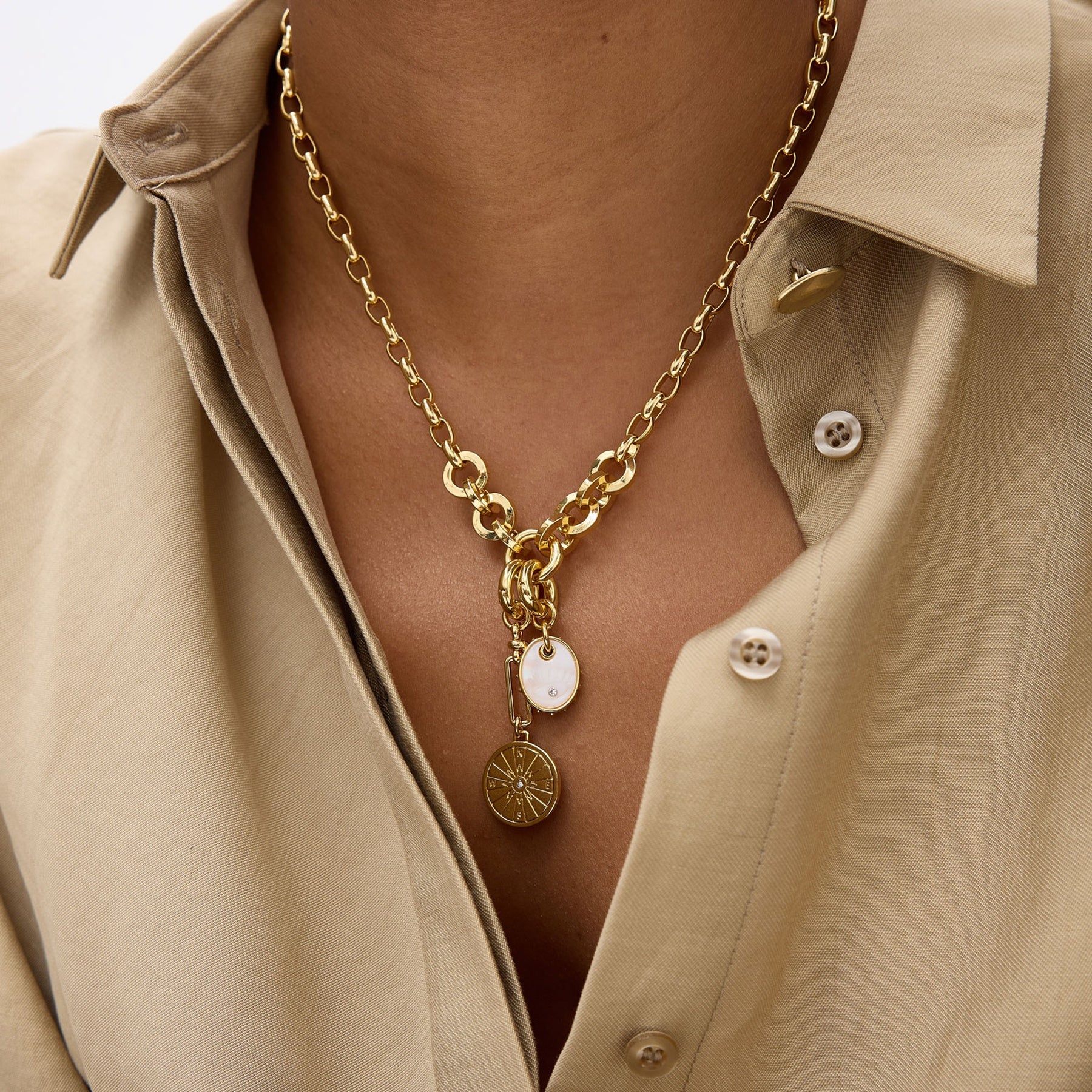 Gold chain necklace with pendants worn by a person in a beige shirt.