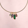 Gold-tone necklace featuring colorful green, blue, and clear pendants along a delicate chain on pink