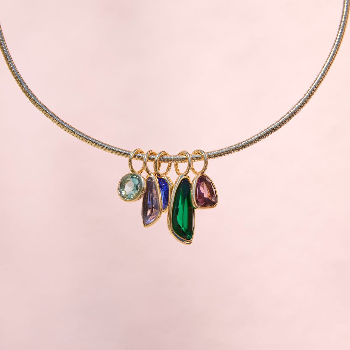 Gold-tone necklace featuring colorful green, blue, and clear pendants along a delicate chain on pink