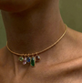 Gold-tone necklace featuring colorful green, blue, and clear pendants along a delicate chain on model closeup 