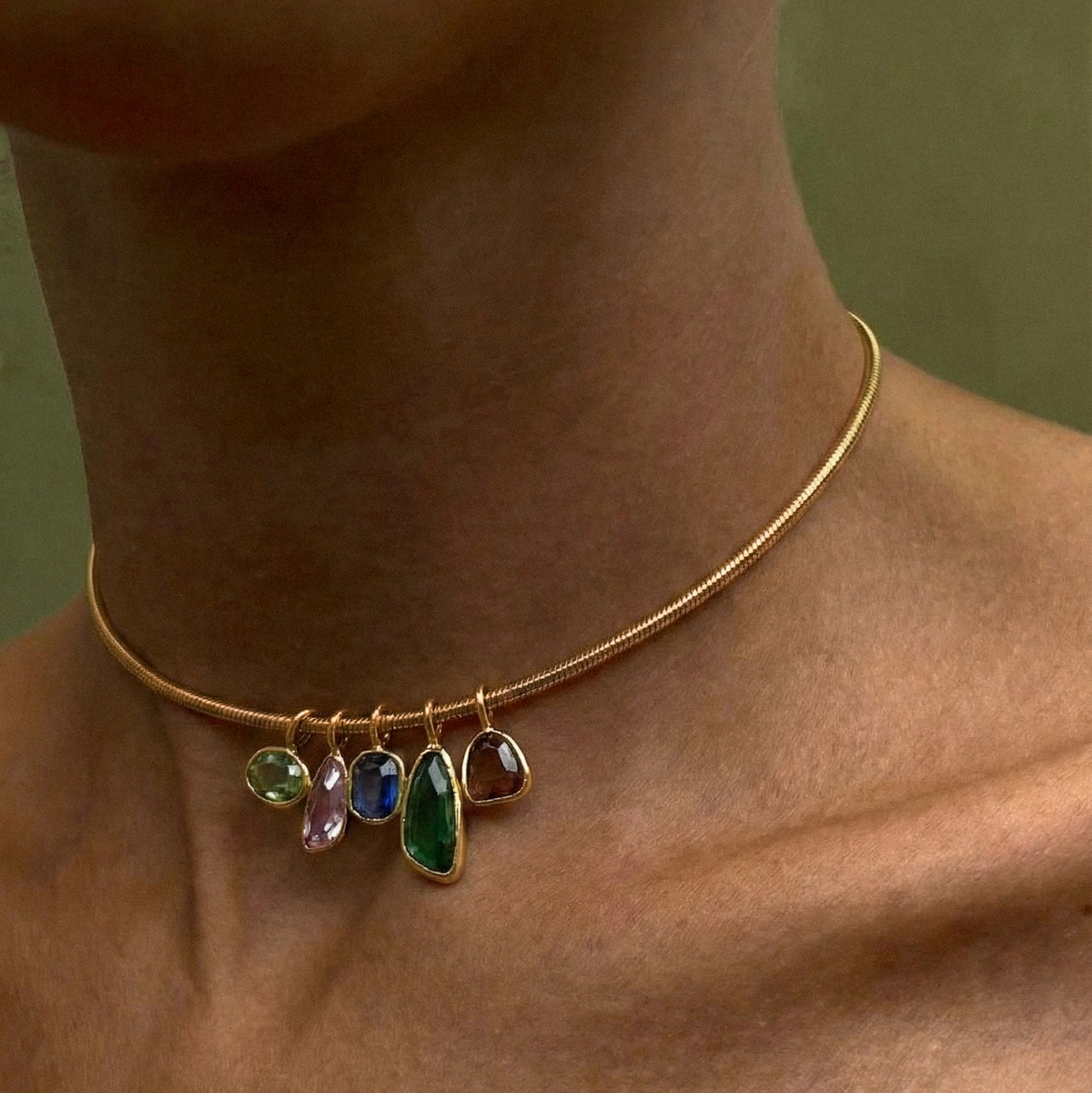 Gold-tone necklace featuring colorful green, blue, and clear pendants along a delicate chain on model closeup 