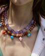Colorful beaded necklace with gemstones on a person wearing a light pink jacket.