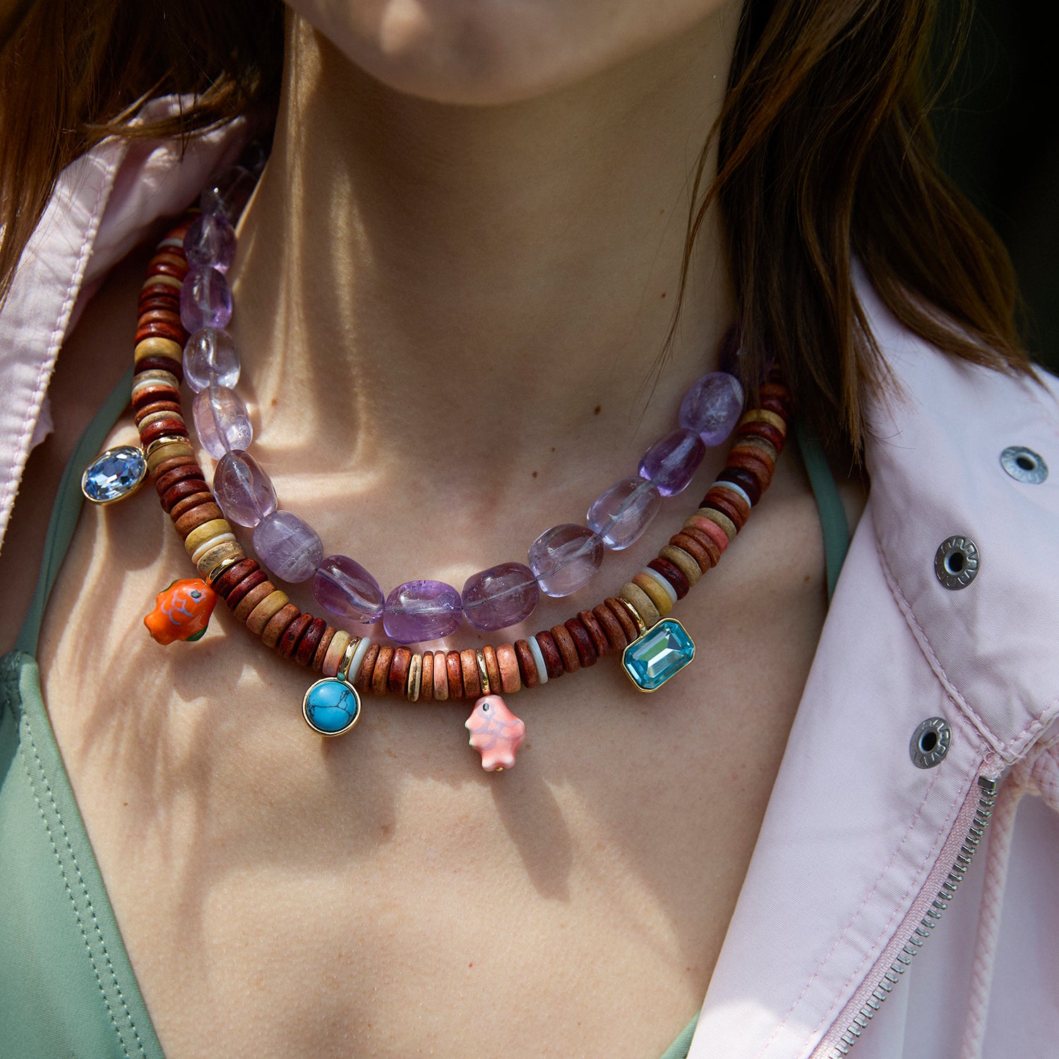 Colorful beaded necklace with gemstones on a person wearing a light pink jacket.
