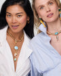 Two women wearing gold necklaces with various pendants on a white background