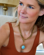 Woman wearing a gold chain necklace with a turquoise pendant indoors.