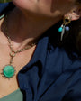 Close-up of a person wearing a gold necklace with a green pendant and a matching earring.